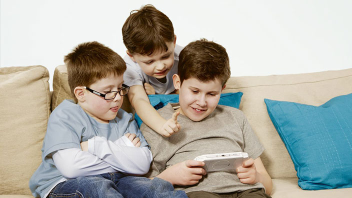 Trois enfants sur un canapé qui s’amusent à des jeux vidéos