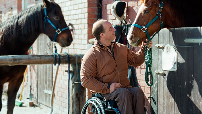 Un homme en fauteuil roulant caressant un cheval