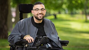 young man in a wheelchair with dark hair and glasses looking at camera